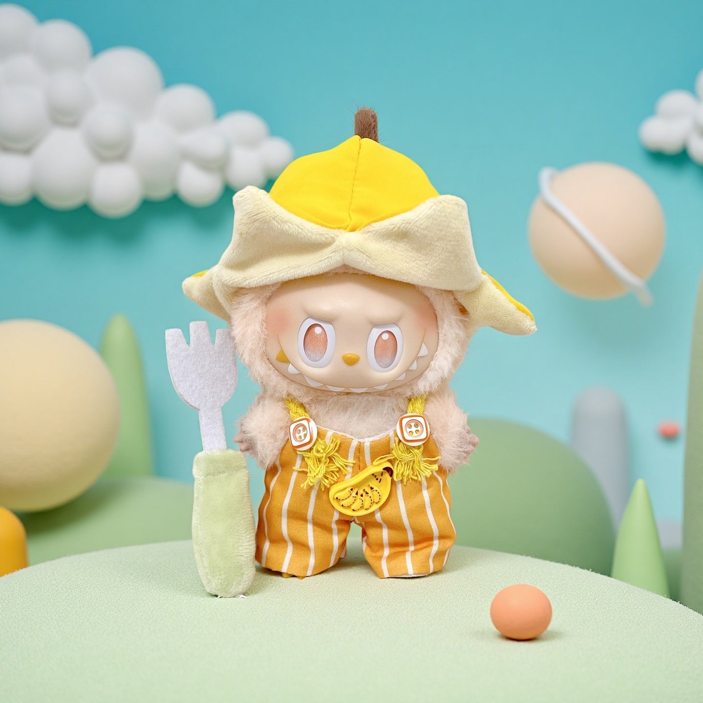 A ZoDoll Labubu Banana Fruit Striped Overalls Outfit with Bucket Hat plush doll stands on a green surface, holding a soft gray fork, with clouds and round objects in the background.