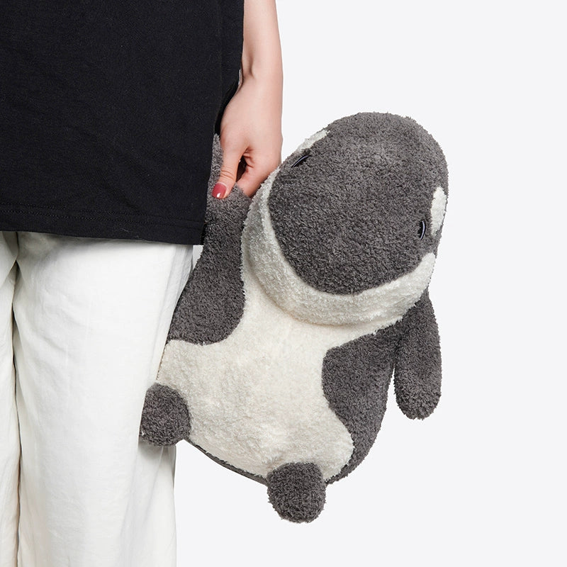 A person in white pants and a black shirt holds the ZEIO Orca Plush Toy 30cm – a soft, cuddly killer whale stuffed animal – against a plain background.