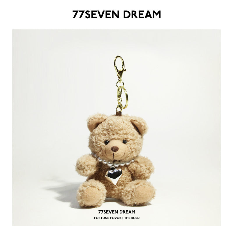Tan bear plush keychain wearing black goggles and a pearl-style necklace with heart pendant