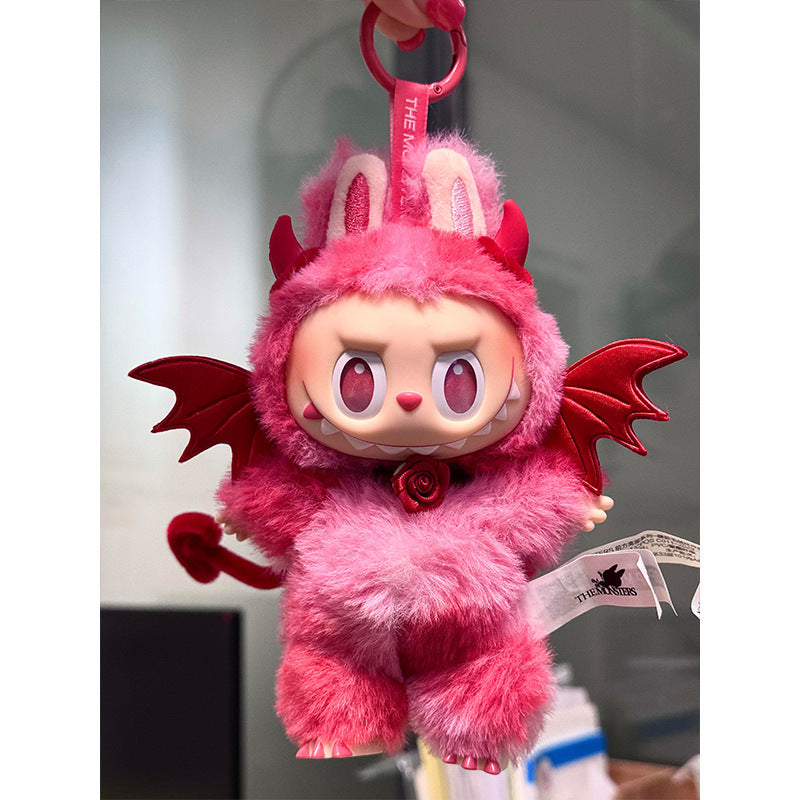 A ZoDoll Labubu Red Devil Bat Wing Fluffy Plush Costume Set keychain features a plush toy with horns, wings, tail, and bunny ears, dressed in a devil bat wing outfit and hanging from a pink keychain indoors.