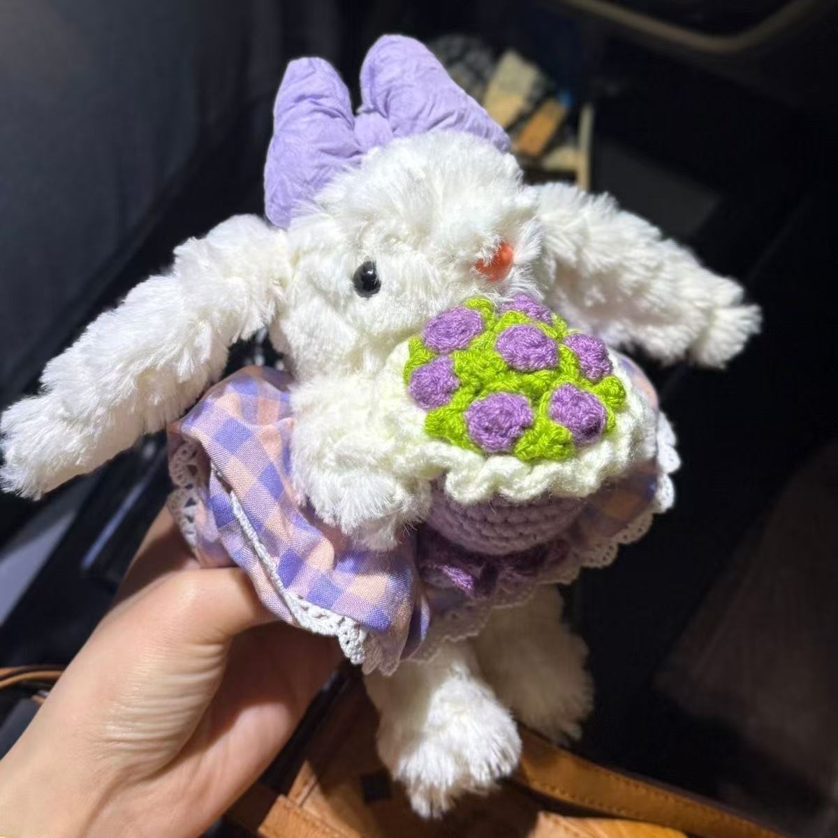 White bunny plush charm with purple bow holding purple flower bouquet with green leaves