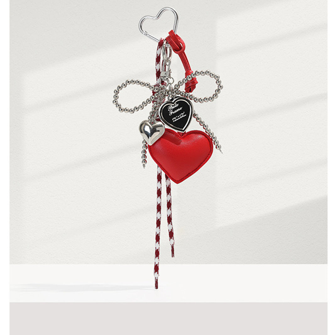 Red faux-leather heart bag charm with pearl bead bow, silver heart accents, and red-and-white striped tassel