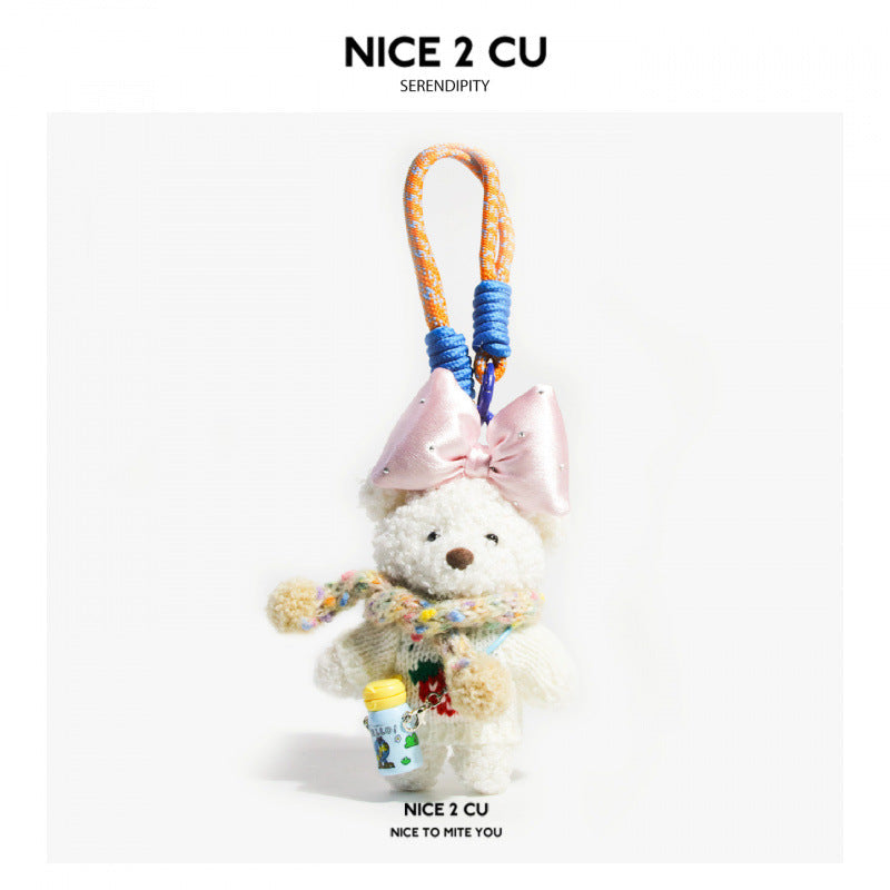 White plush bear charm in light knit outfit with multicolored scarf, pink bow, and small cup-shaped dangling accessory