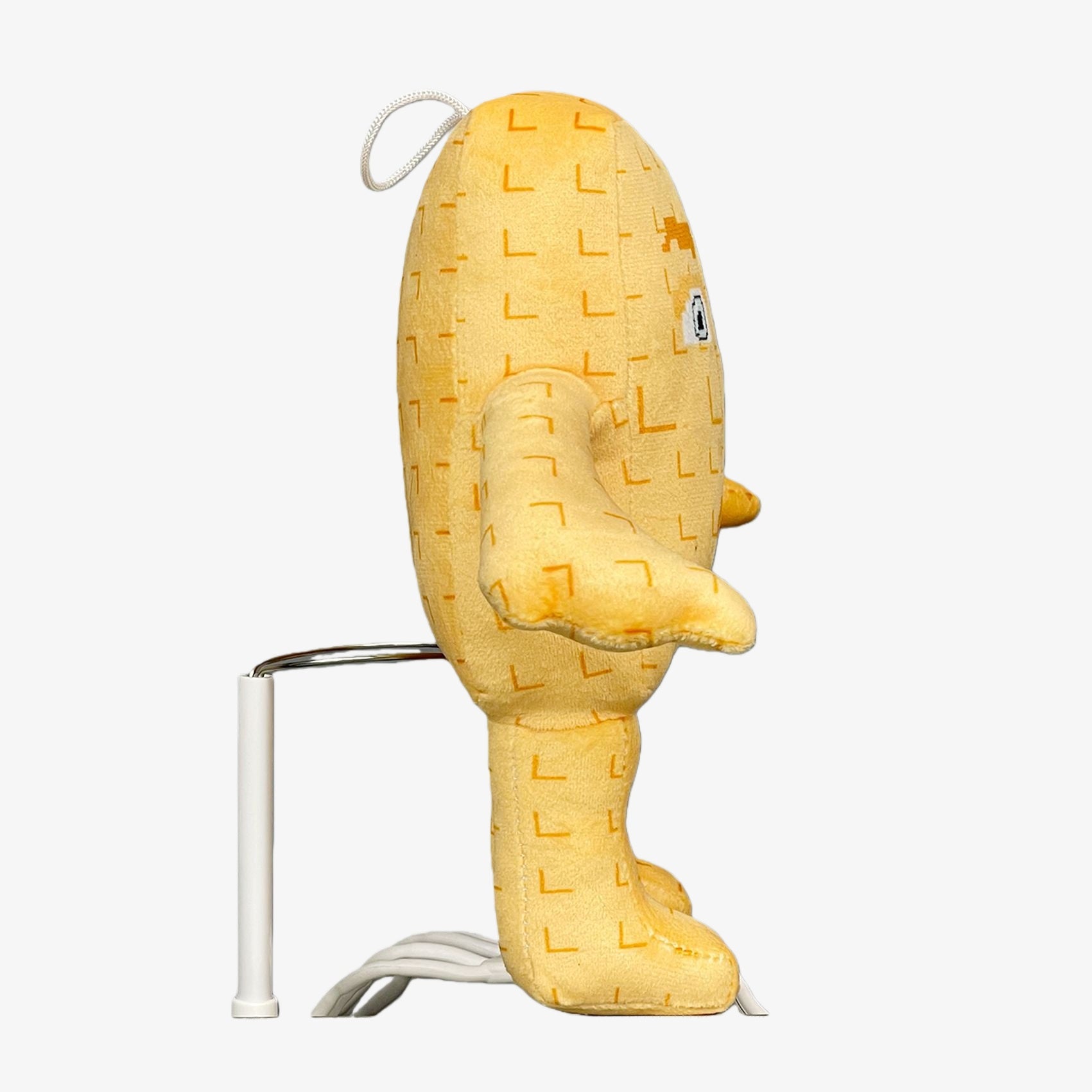 The Steal a Brainrot Inspired Beige Square Character Plush Toy is a 9.1-inch collectible with a pixel face and minimalist design, standing upright in profile on a metal and plastic stand, featuring a white cord extending from its back.