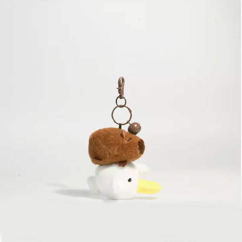 Brown plush capybara keychain posed above a white goose head with yellow beak and metal clip