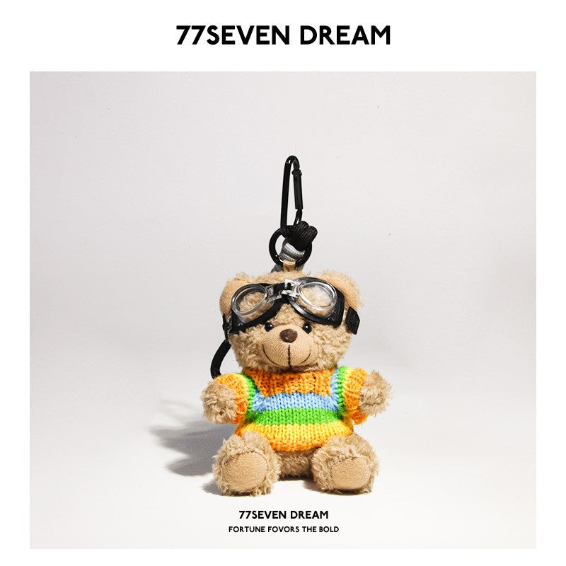 Beige teddy bear plush keychain wearing a multicolor rainbow-striped knit sweater with aviator goggles