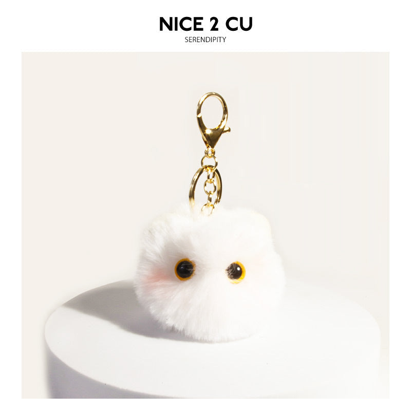Off-white fluffy round cat face keychain charm with dark eyes and gold-tone clip hardware on white display
