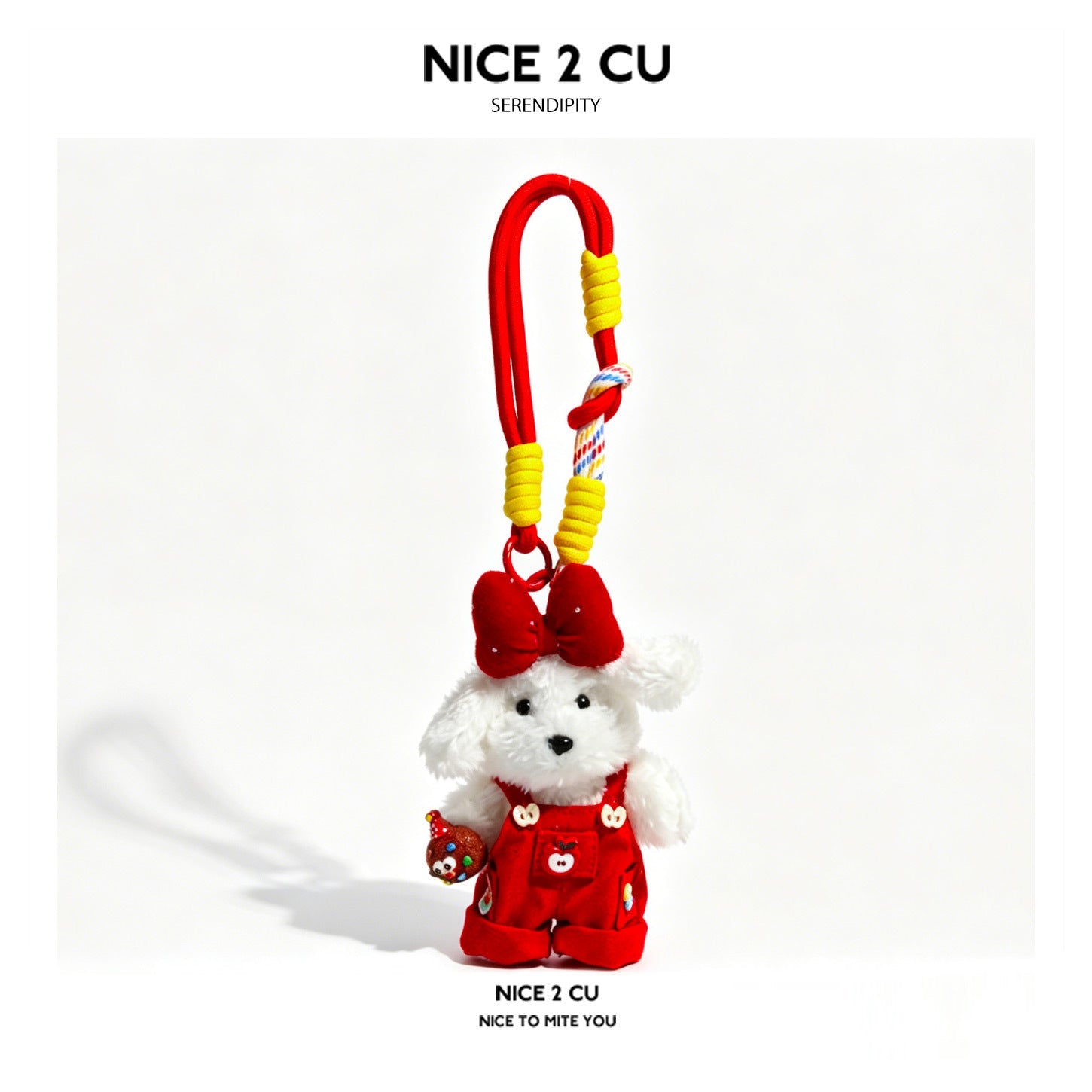 White plush dog charm in red overalls and large red bow, holding a small apple accessory, with red and yellow wrapped cord lo