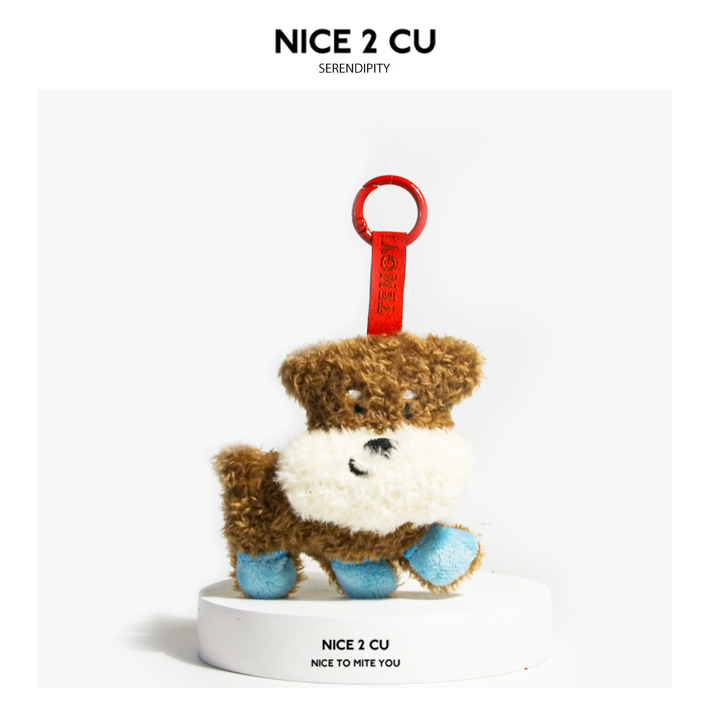Brown and white smiling plush dog charm with blue paw accents and a red loop, displayed on a white base