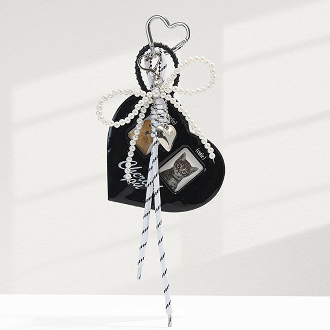 Black heart bag charm with layered pearl bow, two small photo windows, silver heart charm, and striped hanging ribbons
