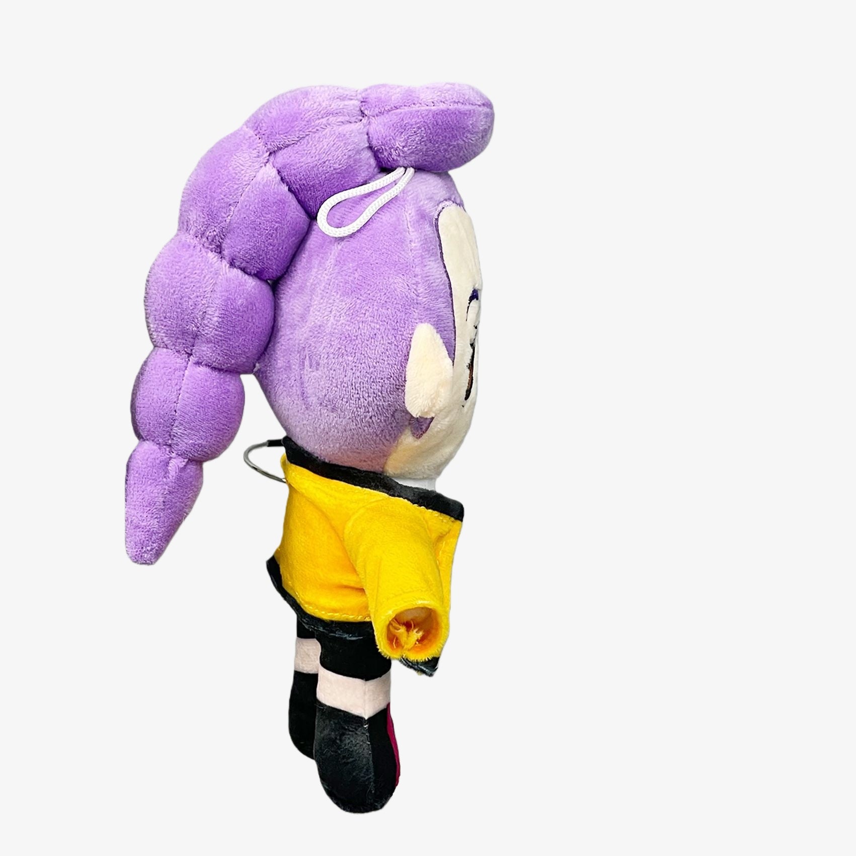 The Demon Hunters Anime Plush Doll is a 9-inch soft stuffed toy featuring a purple-haired female character in a yellow shirt and black shorts, with a hanging loop, shown from the side against a plain white background.