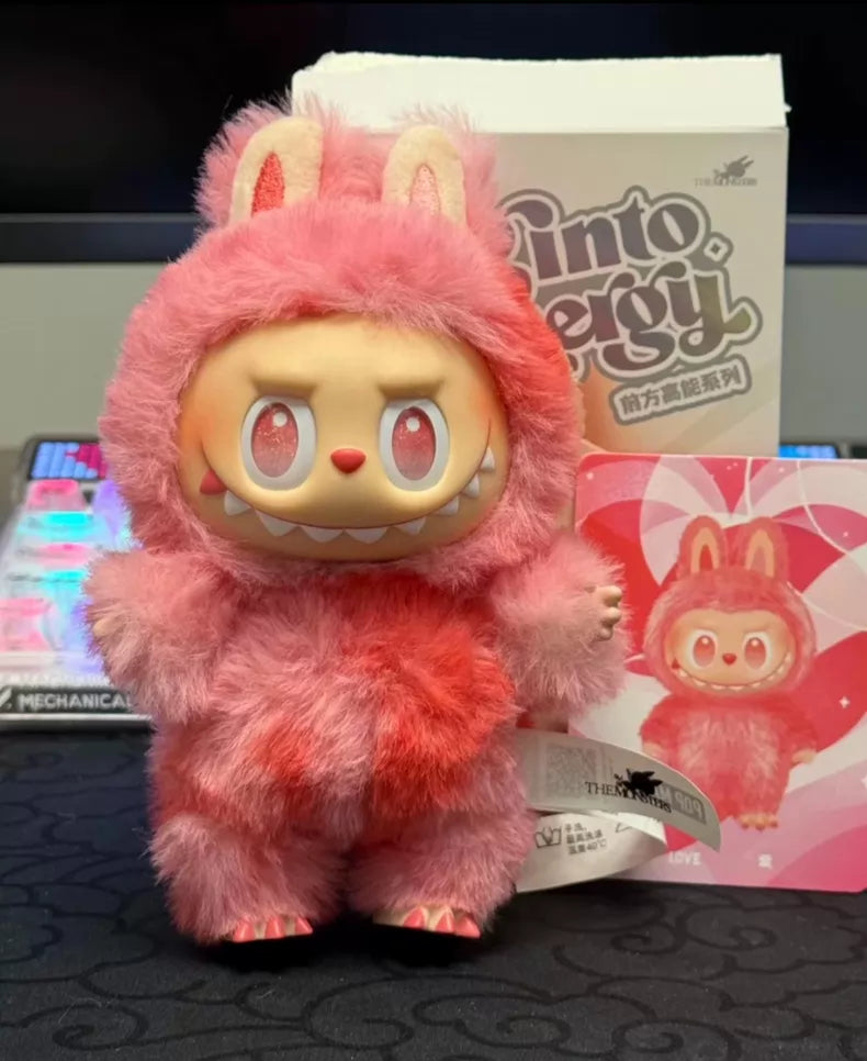 The POP MART Labubu “Love” Plush Keychain – The Monsters “Big Into Energy” Series is a red bunny bag charm with a cartoon face and rabbit ears, shown with its packaging and heart-themed card—a delightful collectible for fans.
