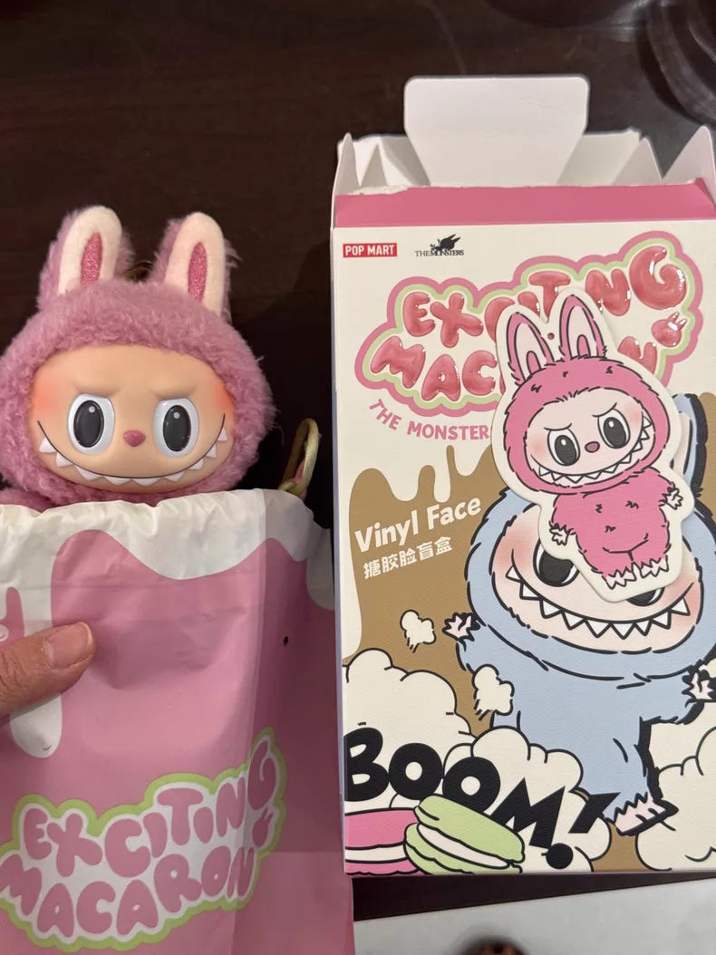 A hand holds the Labubu “Lychee Berry” Plush Keychain—a pink fleece bunny doll by POP MART—inside a pink bag, next to its open packaging with colorful cartoon art and "Exciting Macaron" text, echoing a collectible vibe.