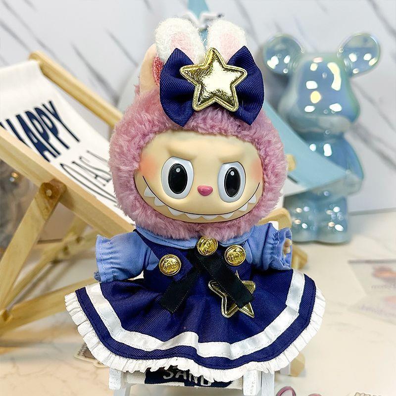 The ZoDoll Labubu Doll wears a navy blue Lolita dress with gold stars and a bow, plus a furry pink bunny-eared hood, and sits before a blue bear figurine and a “Happy” sign.