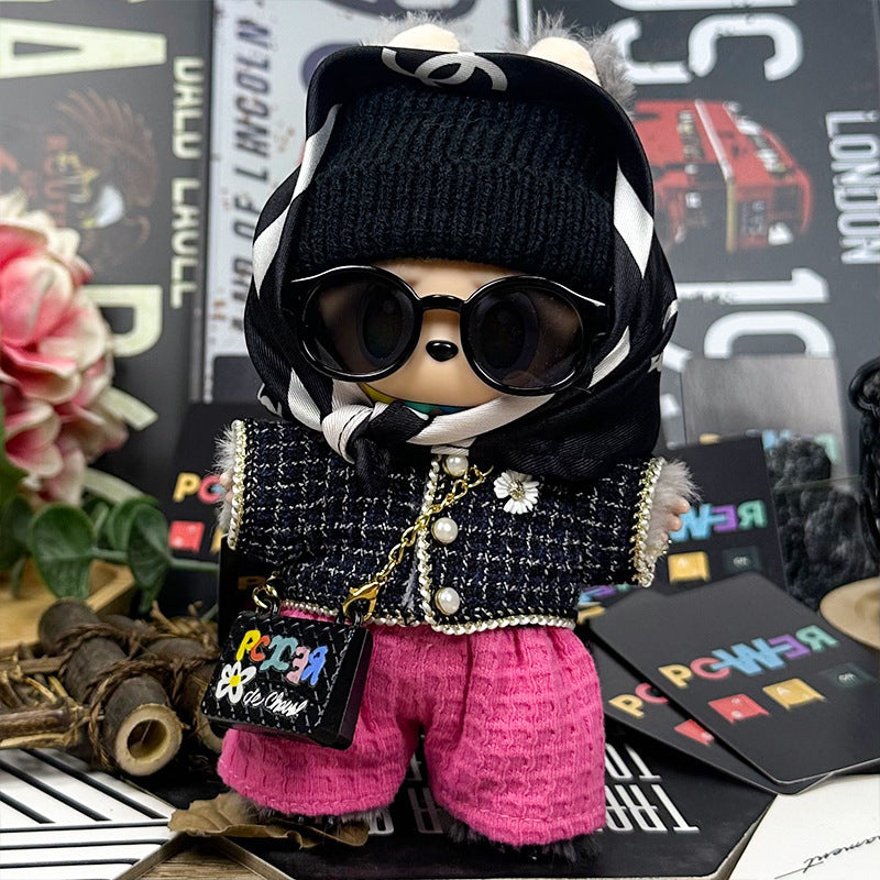 A ZoDoll Labubu plush doll dressed in the Designer Tweed Jacket and Hot Pink Pants Luxury Outfit Set stands amid assorted decorative items, sporting sunglasses, a black beanie, a patterned scarf, brooch, and colorful purse.