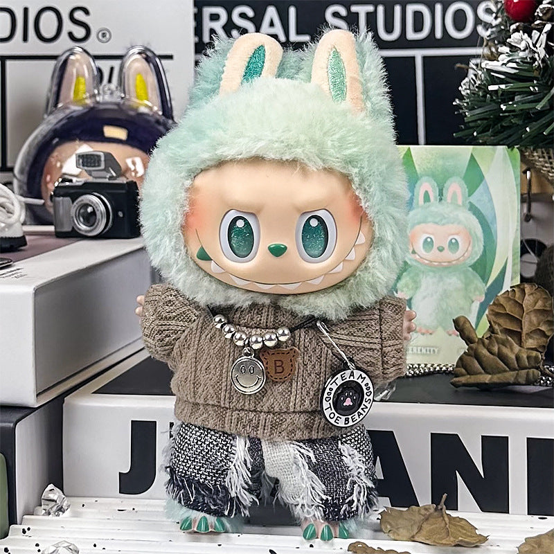 The ZoDoll Labubu Doll Brown Cable Knit Sweater and Fringe Tweed Pants Outfit Set features a doll with big green eyes in a mint-green bunny hood, standing on a shelf with decorations and a toy box behind her.