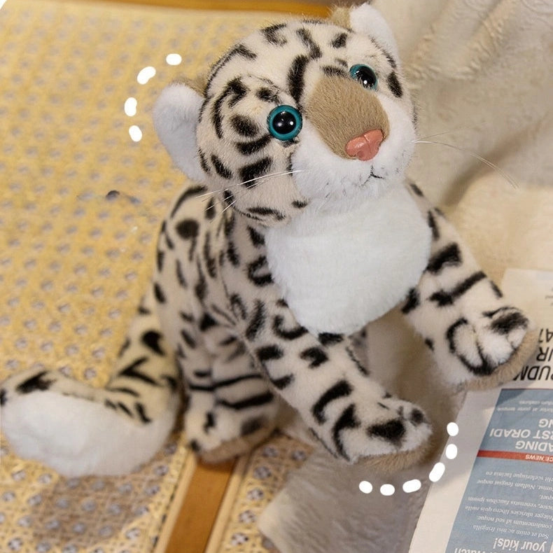 A ZoDoll Snow Leopard Plush Realistic Stuffed Toy (43cm/52cm), white with black spots and teal eyes, sits on a patterned mat beside a piece of paper.