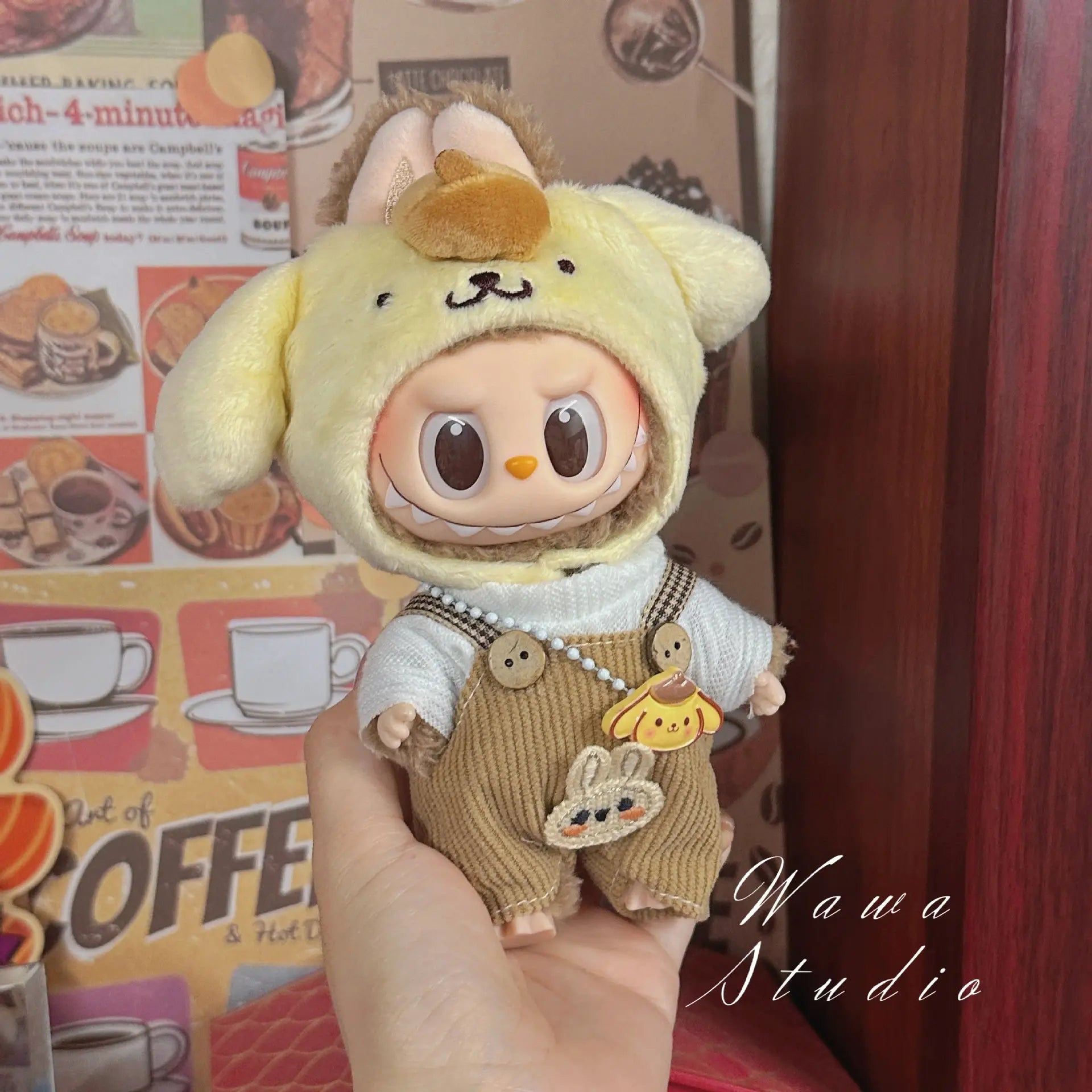 A person holds a ZoDoll Labubu Sanrio Doll dressed in the Hello Kitty Style Outfit Collection in front of a decorated coffee-themed wall.