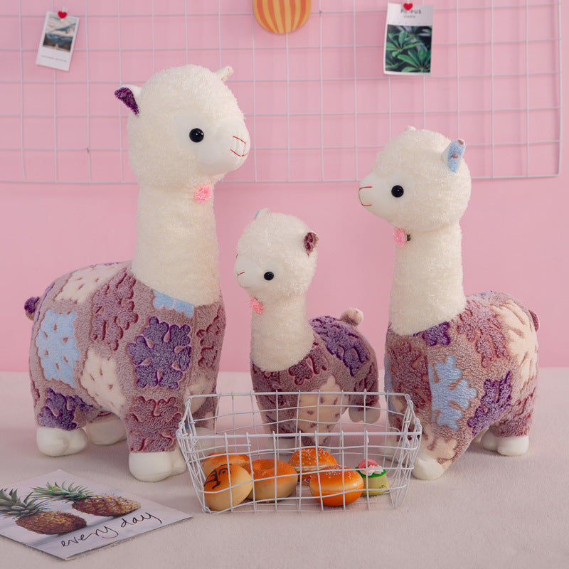 Three ZoDoll Flower Alpaca Plush Toys stand behind a wire basket of toy bread, set against a pink background with a wire grid and cute photos.