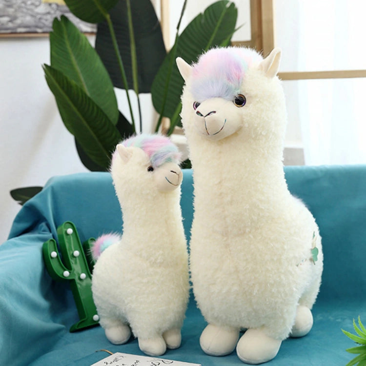 Two ZoDoll Cute Alpaca Plush Toy - Soft Stuffed Alpaca Plush Dolls with pastel tufts are displayed on a blue surface, with a green cactus and leafy plants in the background.
