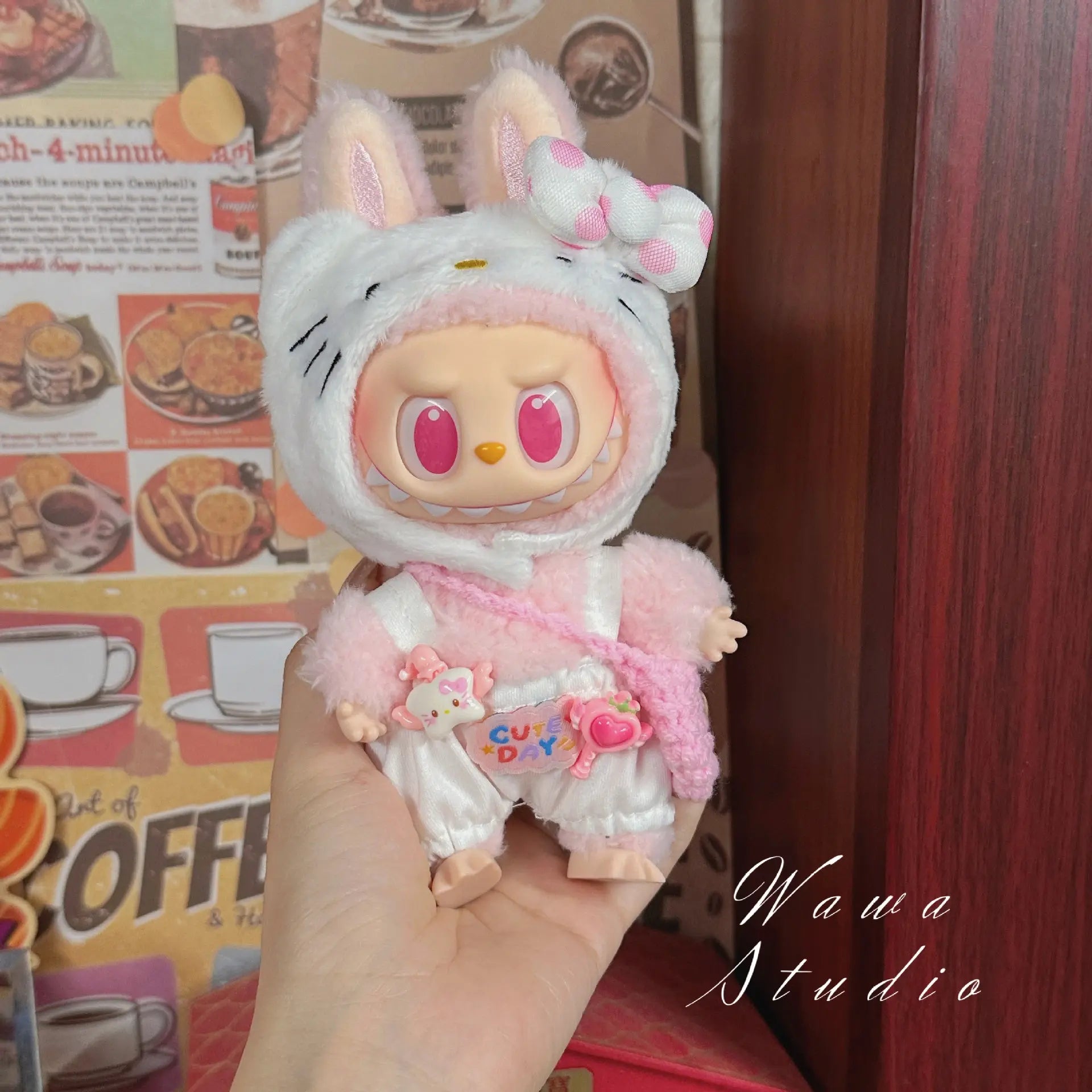 A hand holds a doll in ZoDoll's Labubu Sanrio Doll Clothes Set – Hello Kitty Style Outfit Collection, posed before a retro coffee-themed wall. Wawa Studio appears in the corner.