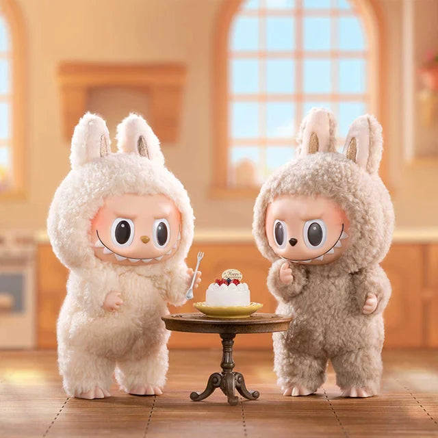 Two plush bunny keychains from the Labubu The Monsters “Exciting Macaron” 6-piece set by POP MART stand by a cake on a table, creating a playful scene in a sunlit kitchen. This limited edition features vinyl face dolls designed for collectors.