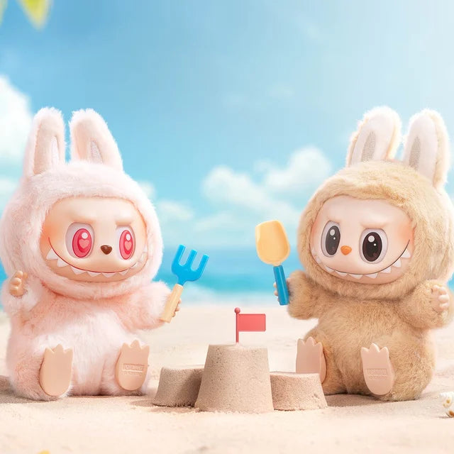 Two plush toys from the POP MART Labubu Have a Seat Series Complete 6-Piece Plush Keychain Set by Pop Mart The Monsters grin with toy tools by a sandcastle, blue sky and clouds creating a playful scene for these cute collectibles.