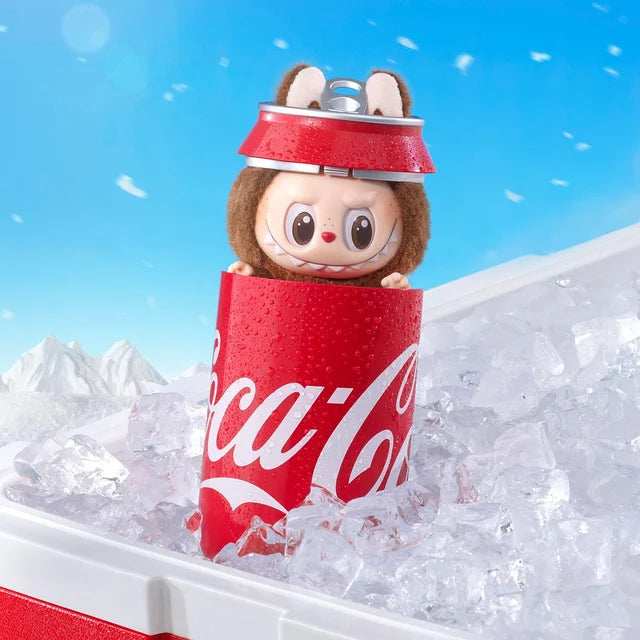 A POP MART Labubu Secret Edition “Mysterious Guest – Coca‑Cola” Plush Keychain sits in an opened Coca‑Cola can atop ice, with snowflakes falling before mountain peaks and a blue sky.