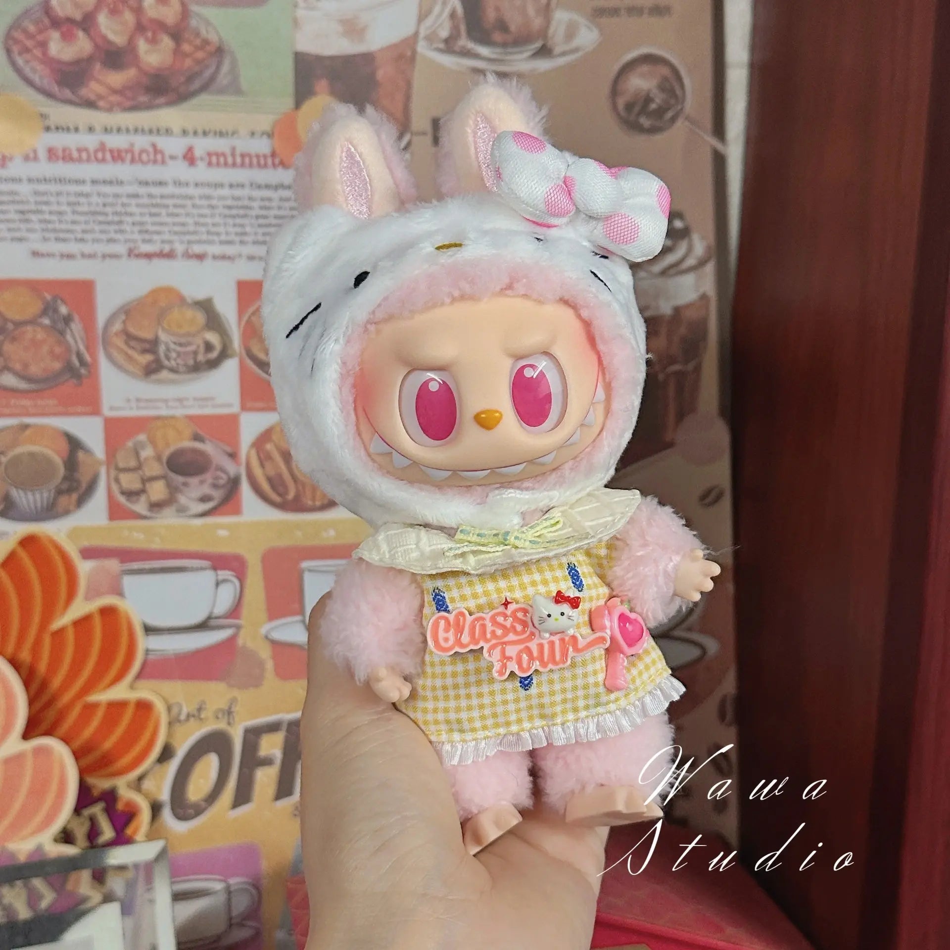 A person holds a pink ZoDoll Labubu Sanrio Doll dressed in a Hello Kitty Style Outfit from the Clothes Set collection; the background displays food images and decorative signs, highlighting kawaii doll fashion.