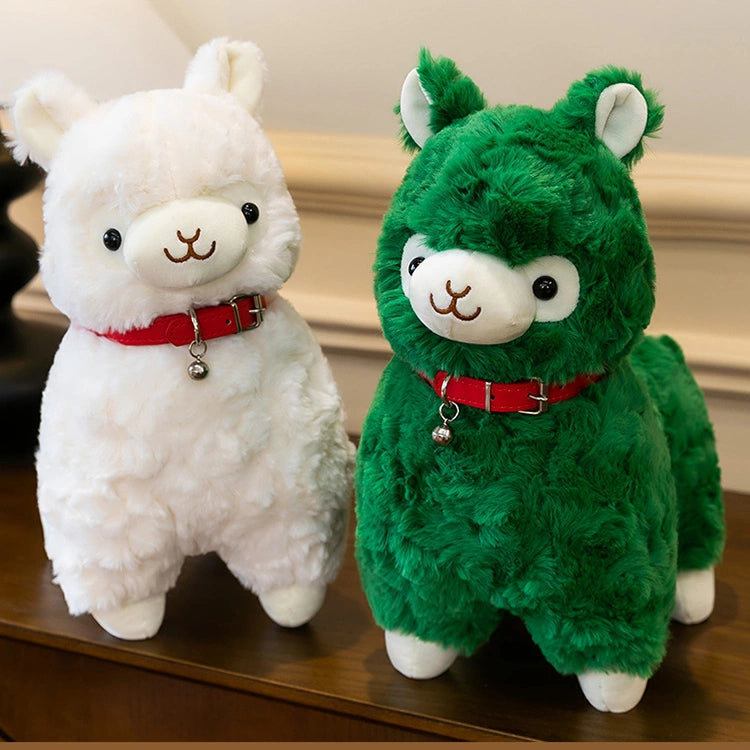 Two ZoDoll Cute Alpaca Plush Toys—a white and a green Soft Stuffed Alpaca Plush Doll, each with a red collar and small bell—stand side by side on a wooden surface.