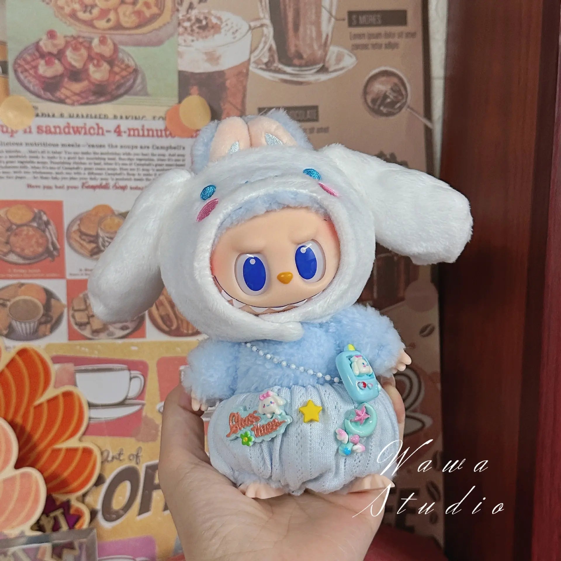 A hand holds a ZoDoll Labubu Sanrio Doll dressed in a Hello Kitty Style Outfit from the new clothes set, standing before a wall decorated with food-themed images and posters.