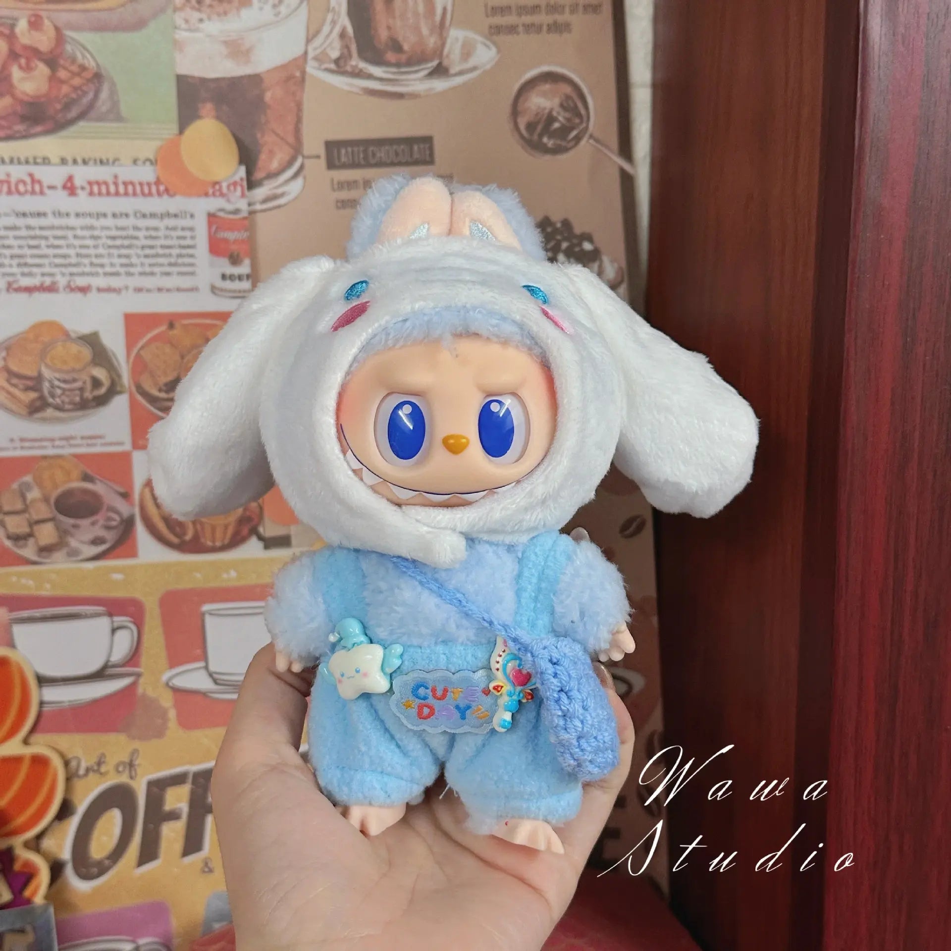 A ZoDoll Labubu Sanrio Doll wears a Hello Kitty Style Outfit from the official collection, inspired by kawaii fashion, standing before a retro café poster. The Wawa Studio text appears in the bottom right corner.