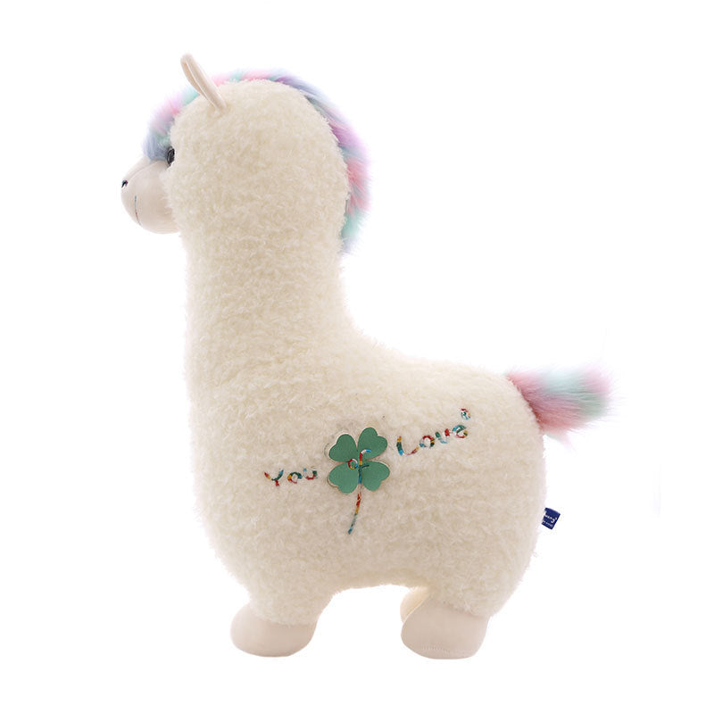 The ZoDoll Cute Alpaca Plush Toy is a soft stuffed alpaca doll with white fur, a pastel rainbow mane and tail, and a green clover embroidered with "You Love" on its side.