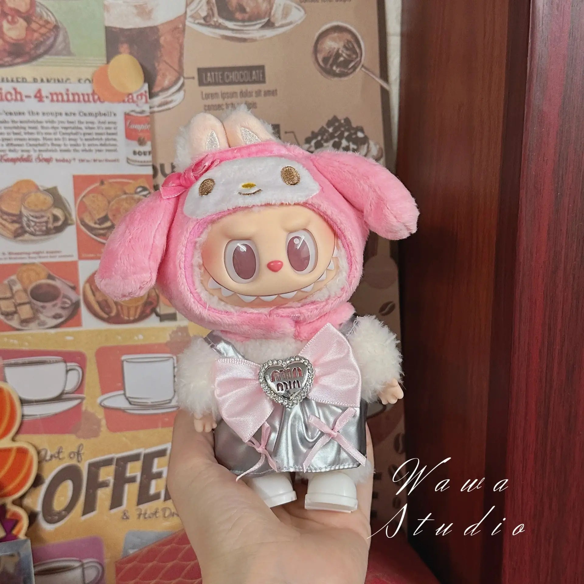 A hand holds a ZoDoll Labubu Sanrio Doll Clothes Set – Hello Kitty Style Outfit, featuring kawaii fashion, against coffee-themed decor with "Yawa Studio" in the corner.