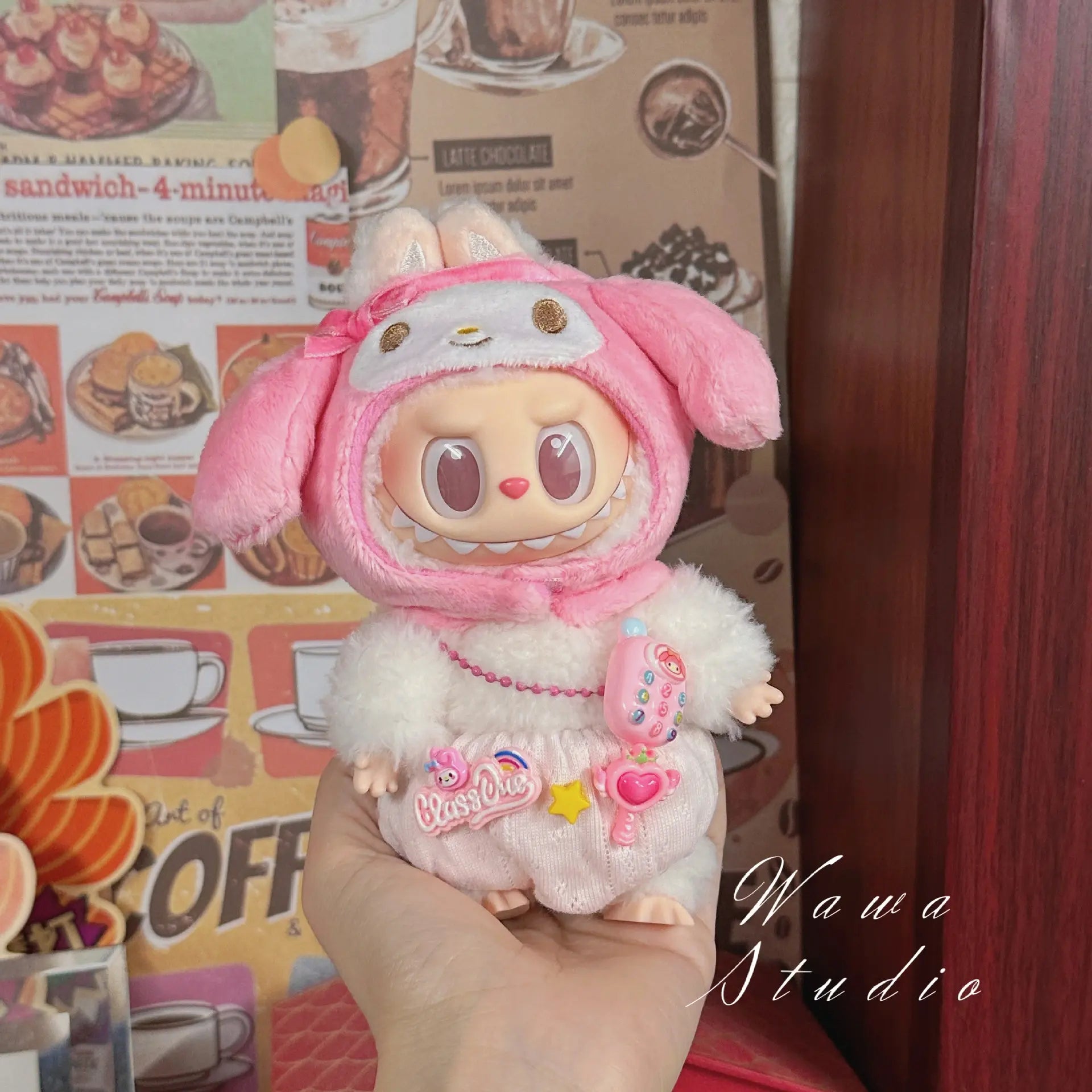 A hand holds a ZoDoll Labubu Sanrio Doll wearing the Hello Kitty Style Outfit from the ZoDoll Labubu Sanrio Doll Clothes Set, set against a vibrant retro cafe poster background.