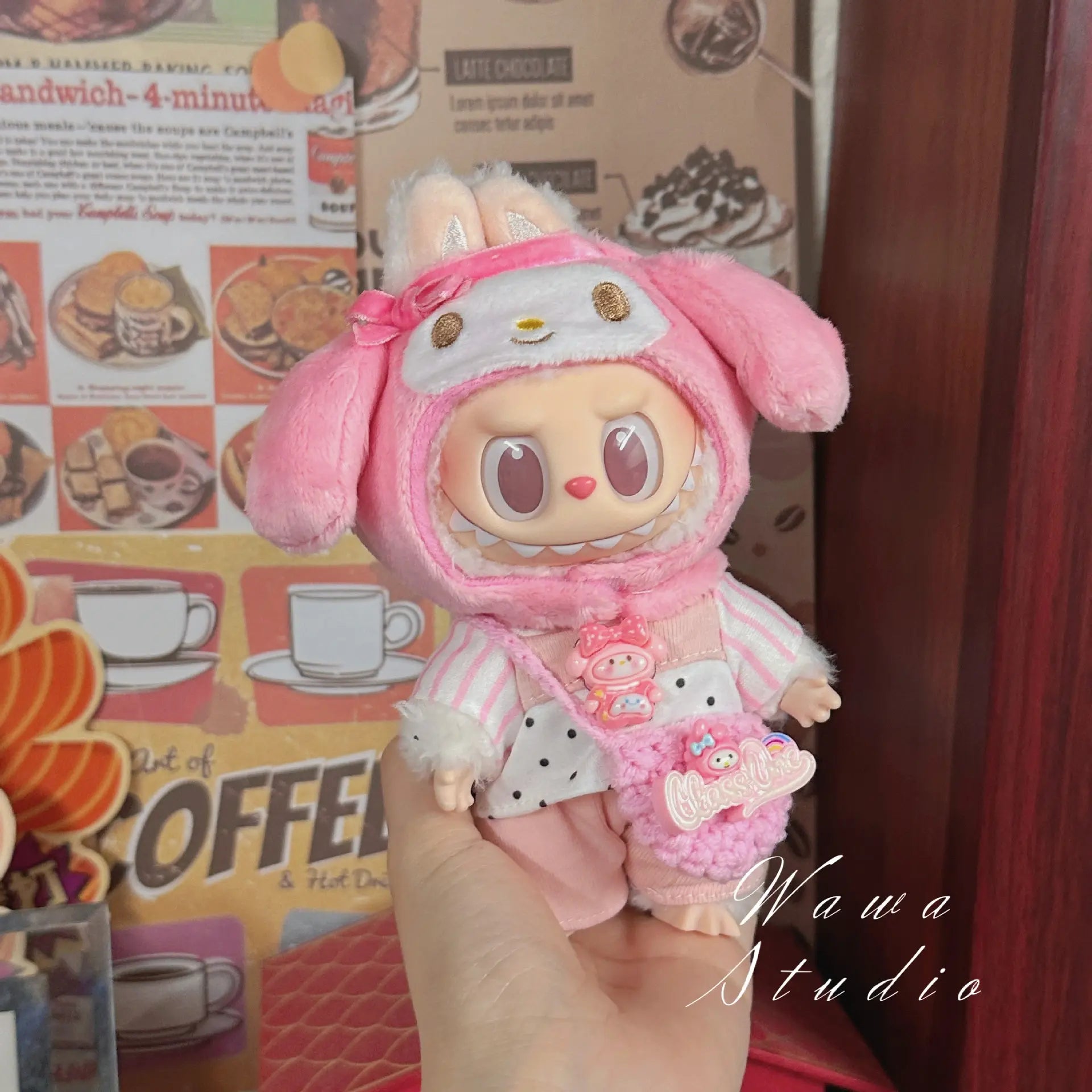 A hand holds a ZoDoll Labubu Sanrio Doll Clothes Set, featuring a Hello Kitty style outfit, with kawaii fashion accents and café decor plus a coffee poster in the background.