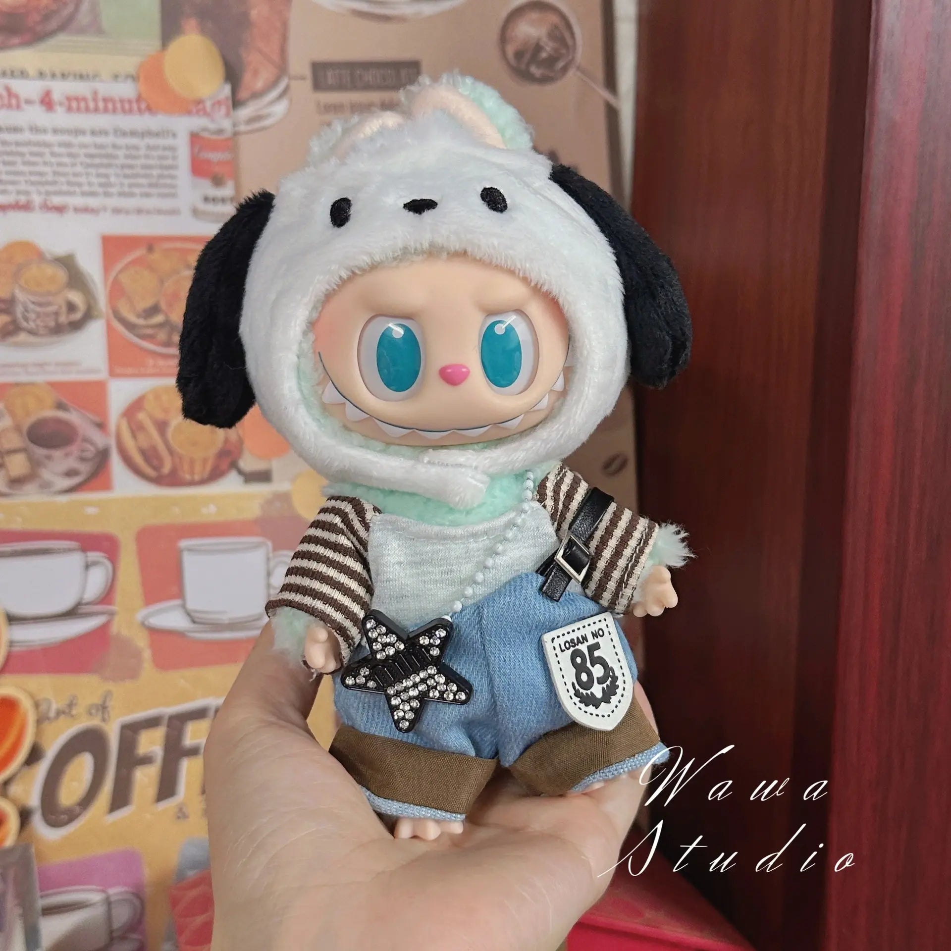A person holds a wide-eyed ZoDoll dressed in the Labubu Sanrio Doll Clothes Set – Hello Kitty Style Outfit Collection, with food-themed wall decor in the background.
