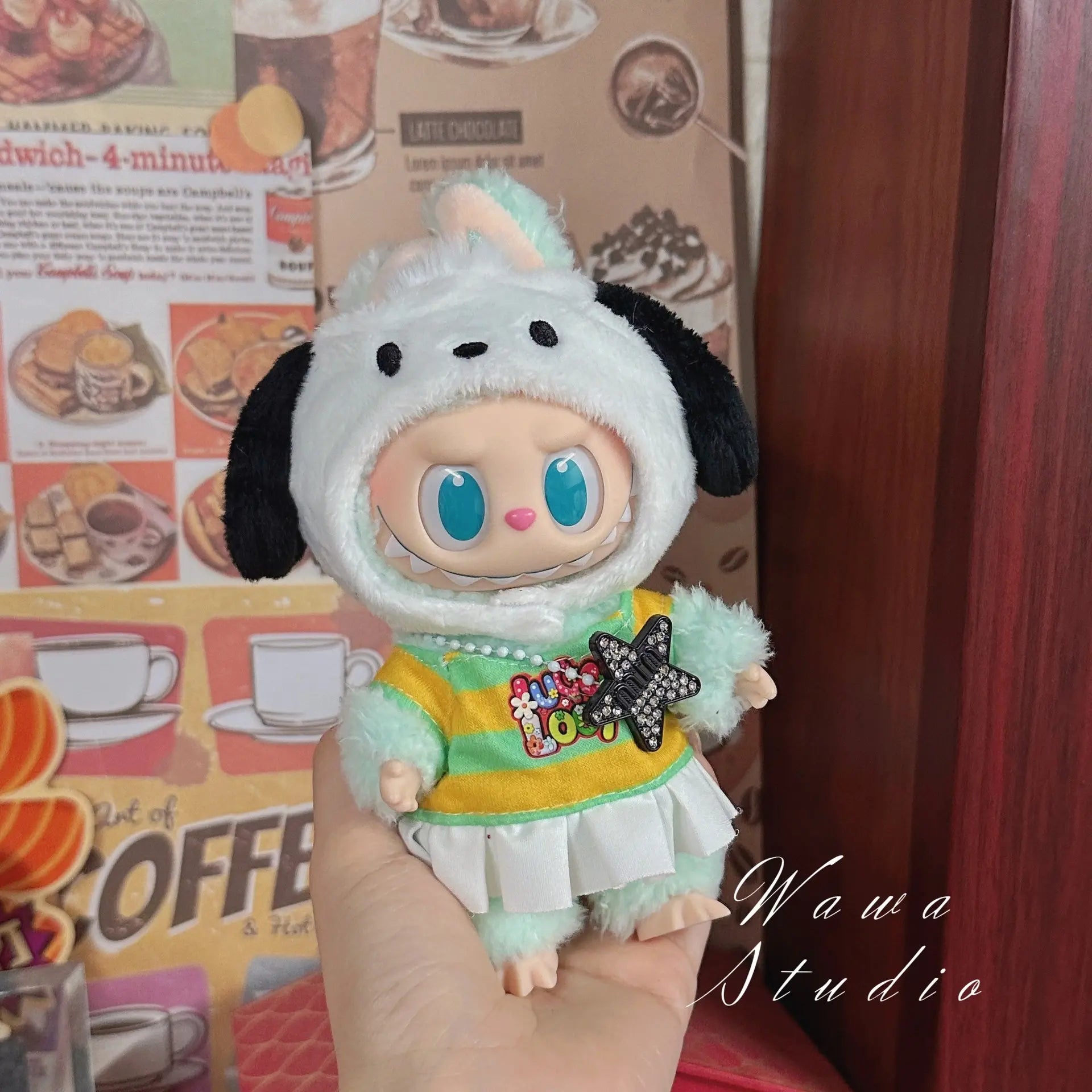 A hand holds a ZoDoll Labubu Sanrio Doll Clothes Set featuring a Hello Kitty style outfit. The background shows a colorful menu and the words Wawa Studio.