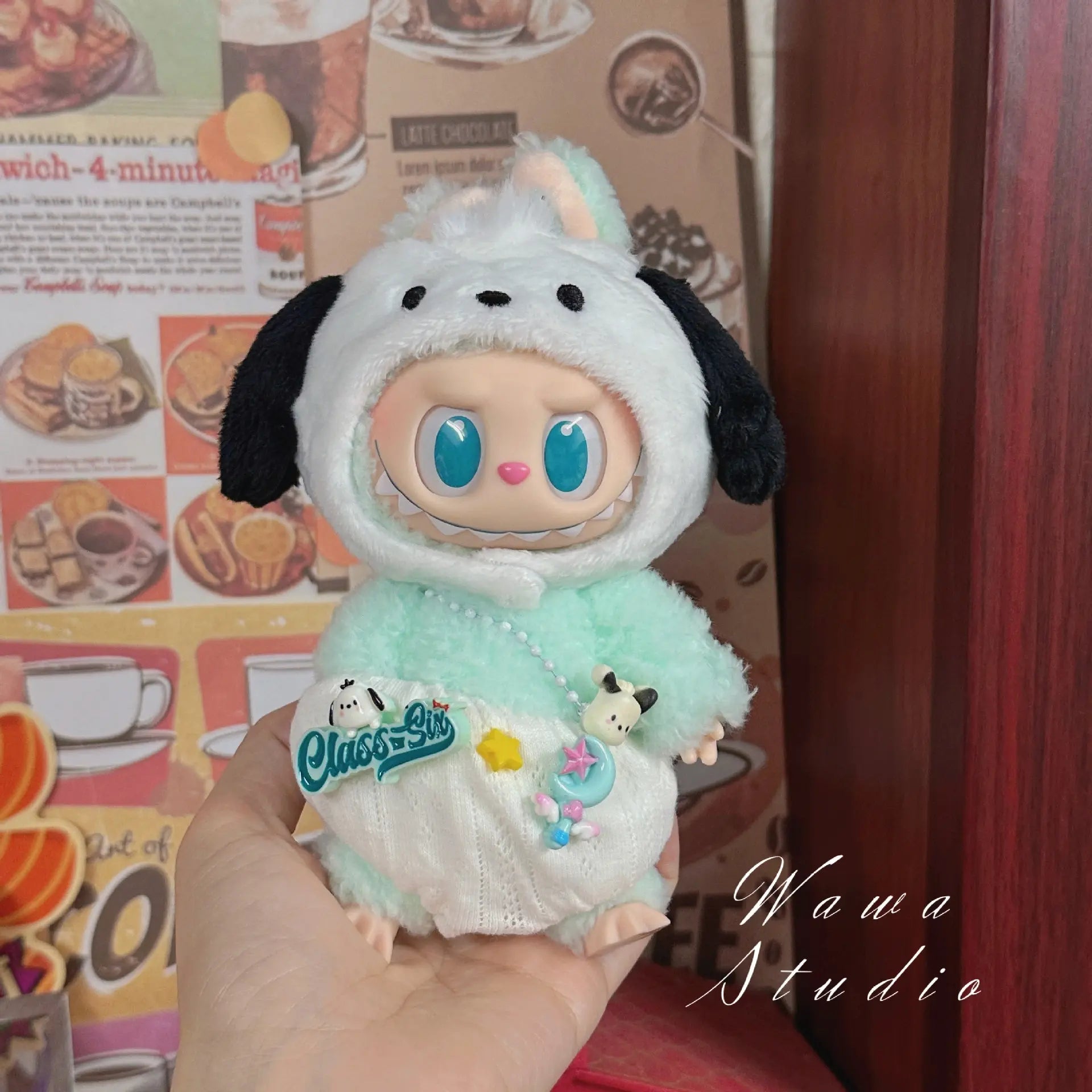A hand holds a ZoDoll Labubu Sanrio Doll Clothes Set figure in a Hello Kitty-style mint green outfit with a hood and blue eyes, set against a cafe-themed background. “Wawa Studio” appears at the bottom right.