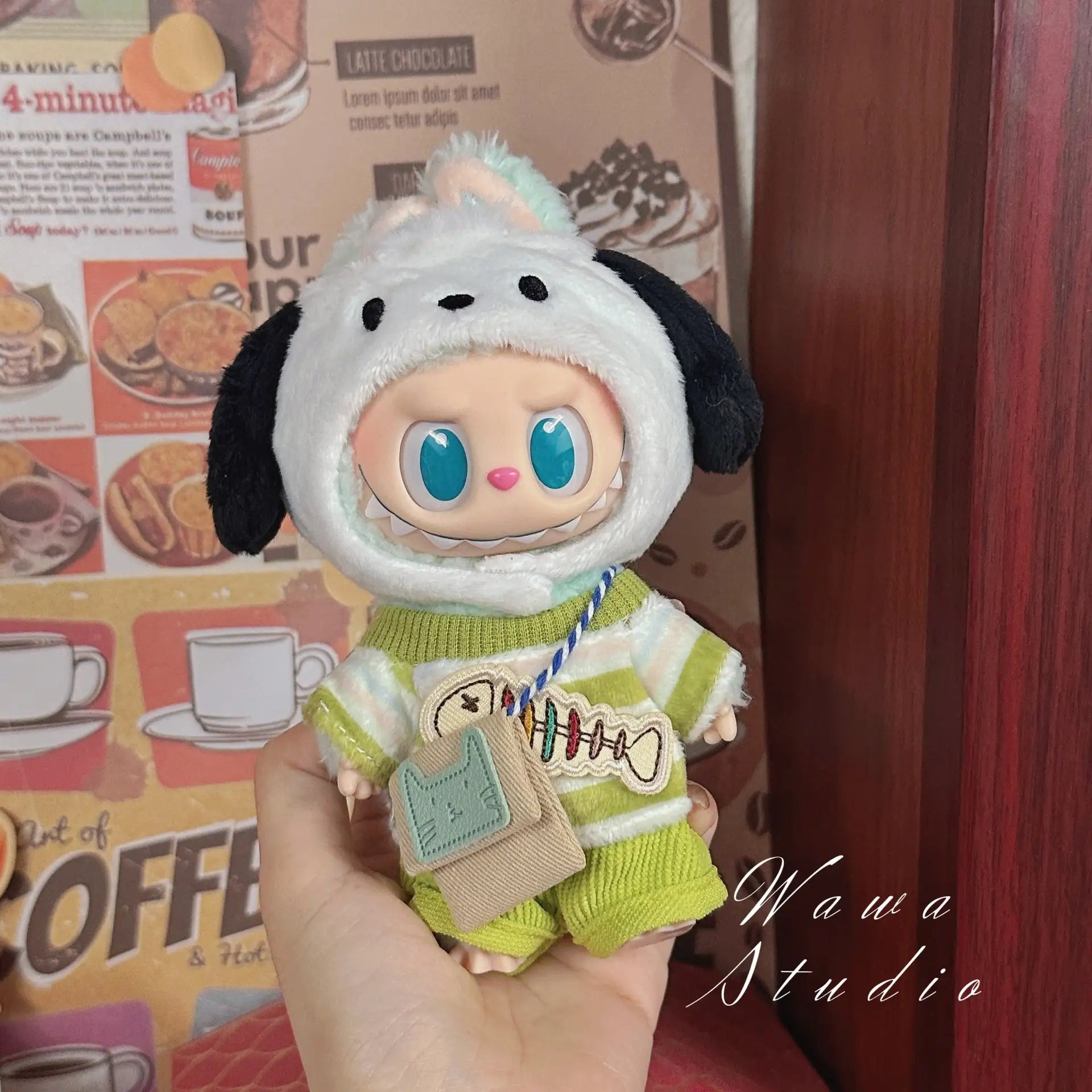 A hand holds a ZoDoll Labubu Sanrio Doll in a Hello Kitty Style Outfit from the Clothes Set collection, showcasing kawaii doll fashion. Coffee-themed wall art decorates the background, with "Wawa Studio" in the corner.