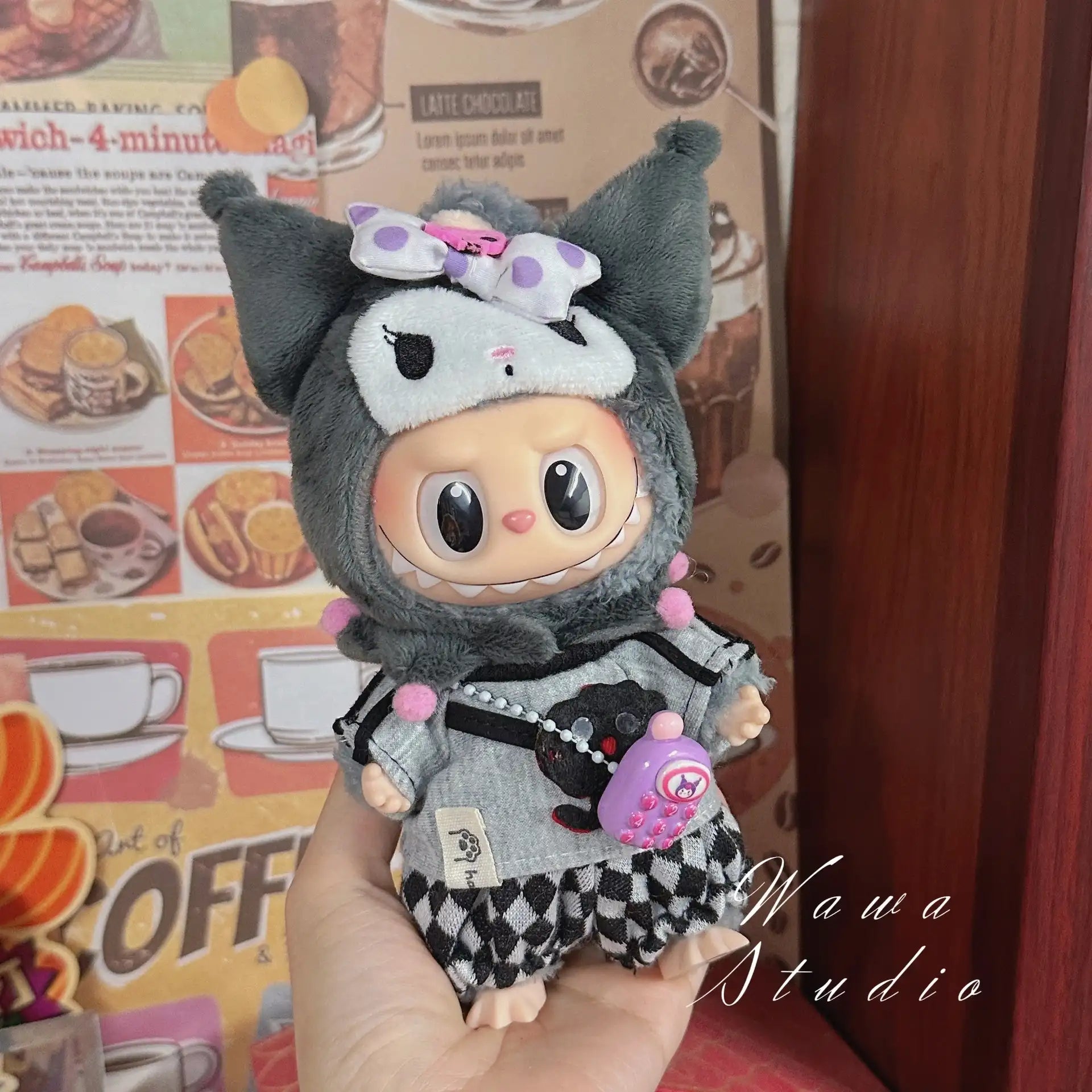 A ZoDoll Labubu Sanrio Doll wears a Hello Kitty style outfit from the Outfit Collection; the kawaii ensemble stands out against a colorful food-themed background and wooden surface as it’s held in a hand.