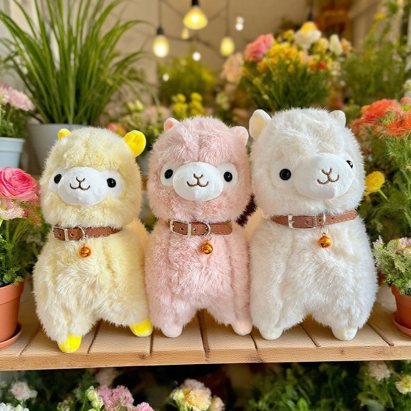 Three ZoDoll Cute Alpaca Plush Dolls—yellow, pink, and white—stand together on a wooden shelf, surrounded by potted plants and flowers.