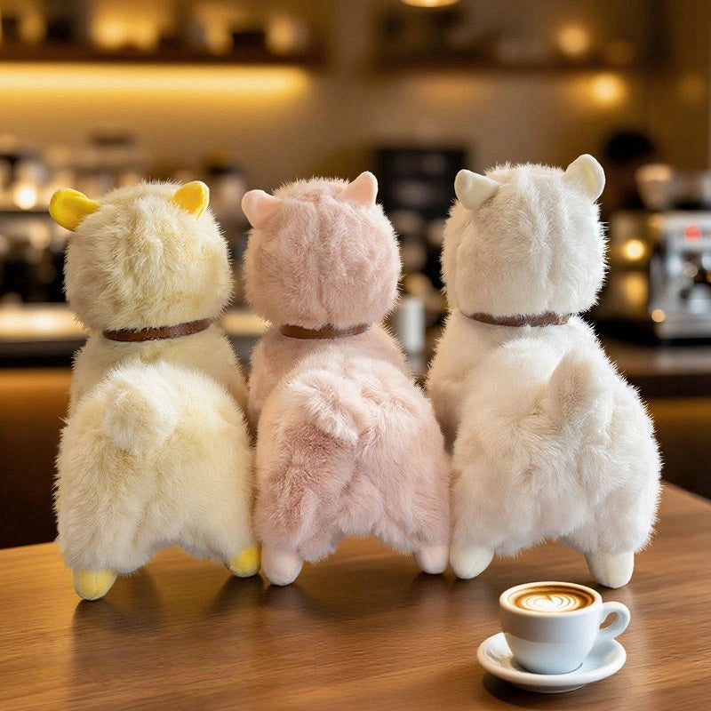 Three ZoDoll Cute Alpaca Plush Doll - Soft Alpaca Plush Toys stand side by side on a wooden table, facing away, with a latte art coffee in front of them, set in a warmly lit café.