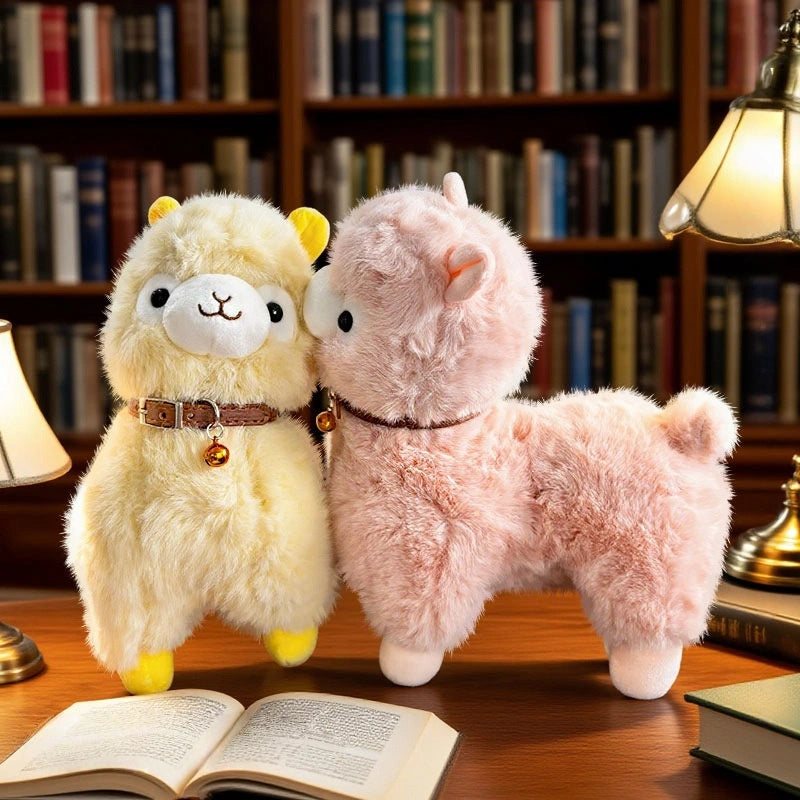 Two ZoDoll Cute Alpaca Plush Dolls—one yellow, one pink—stand on a desk with an open book, surrounded by bookshelves and warm lamps in a cozy library setting.