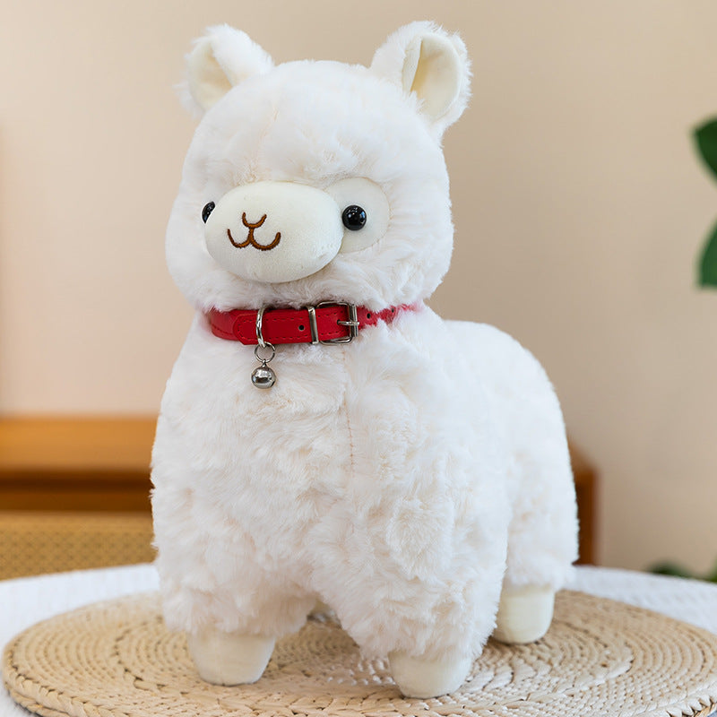 The ZoDoll Cute Alpaca Plush Toy, a soft stuffed alpaca plush doll with a red collar and bell, stands on a woven mat indoors, bringing adorable charm to any space.
