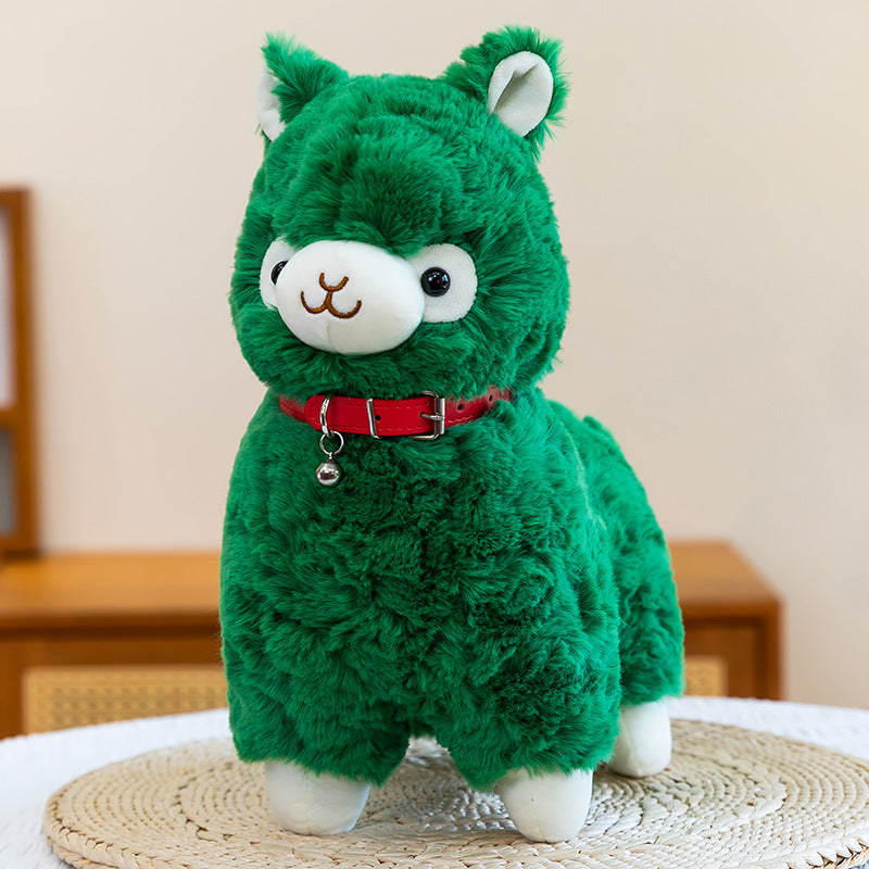The ZoDoll Cute Alpaca Plush Toy is a soft stuffed alpaca plush doll with a green body, white feet and face, and a red collar with a silver bell, shown sitting on a woven mat indoors.