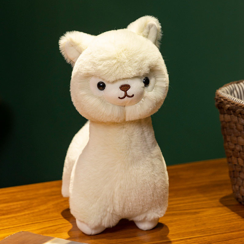 The ZoDoll Cute Alpaca Plush Doll, a soft alpaca plush toy with cream fur, sits on a wooden surface beside a woven basket against a dark green background.