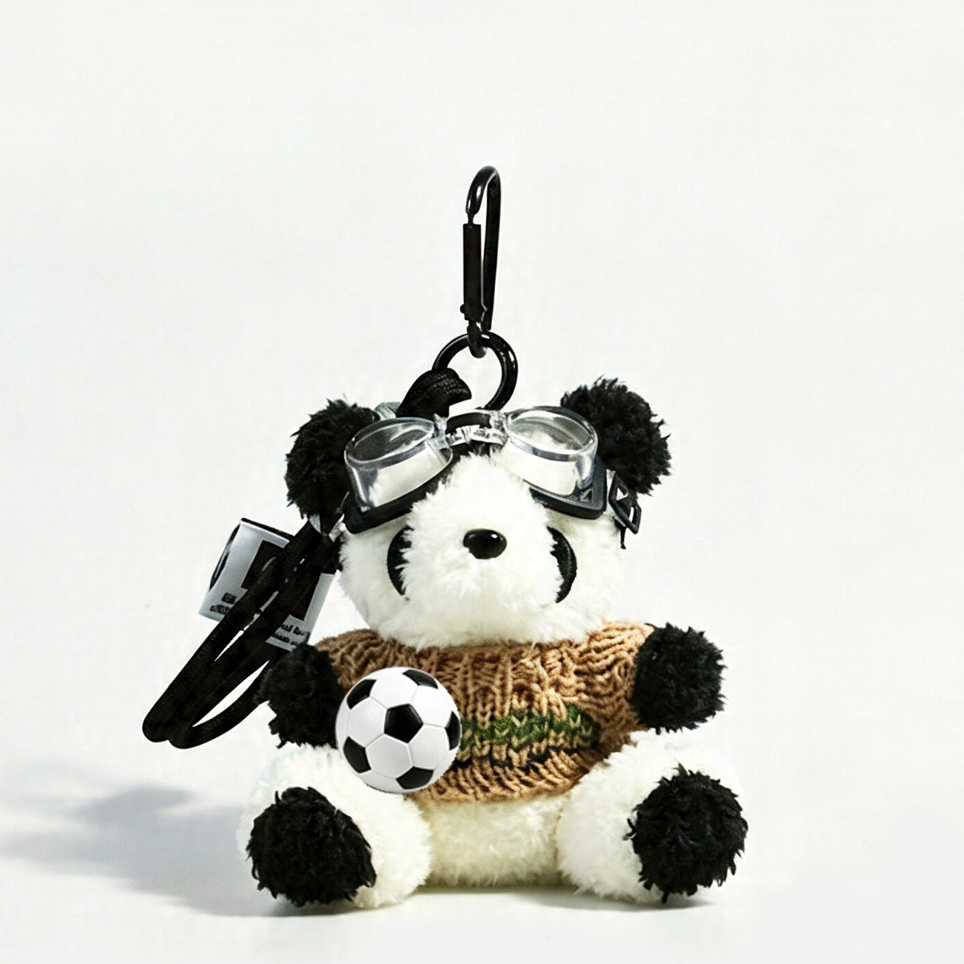 Panda plush charm wearing a khaki brown striped knit sweater, goggles pushed up on forehead, holding soccer ball