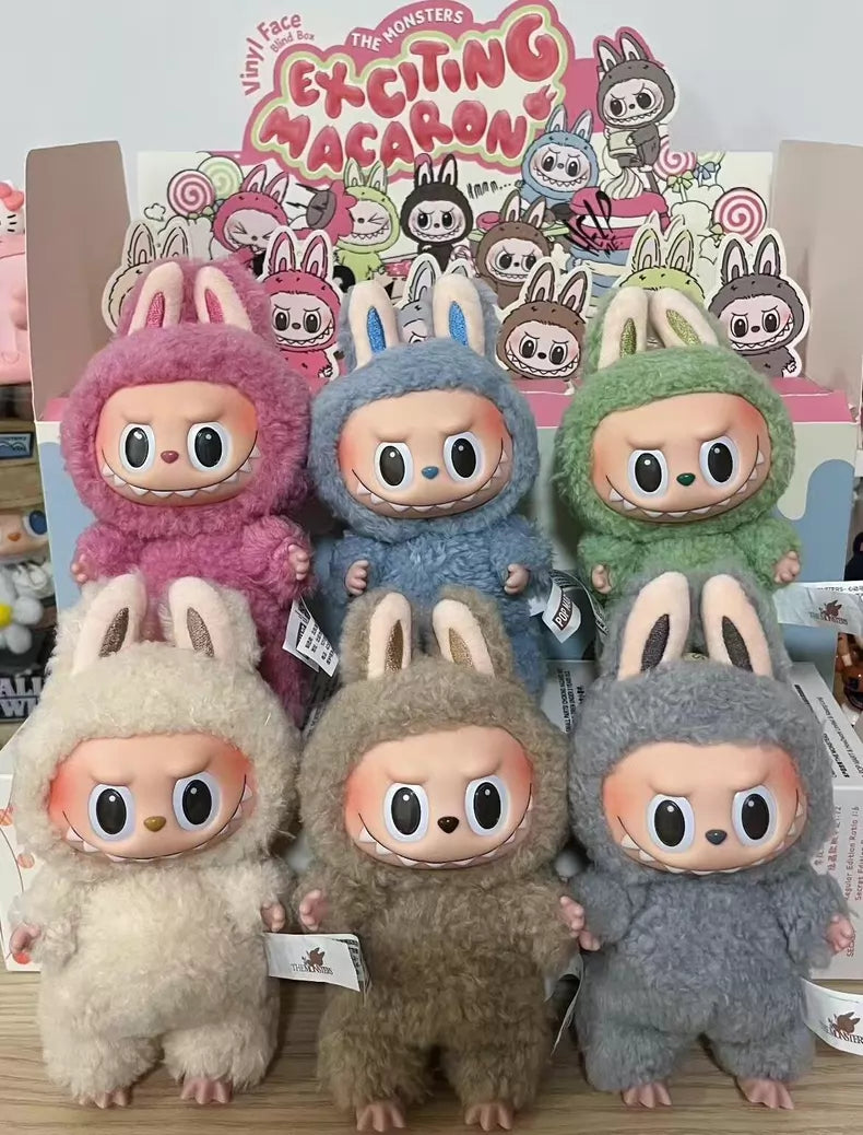 Six pastel plush keychains with bunny ears and vinyl faces from the POP MART Labubu The Monsters “Exciting Macaron” 6-Piece Plush Keychain Set are displayed before a colorful sign, showcasing this limited edition collectible set.