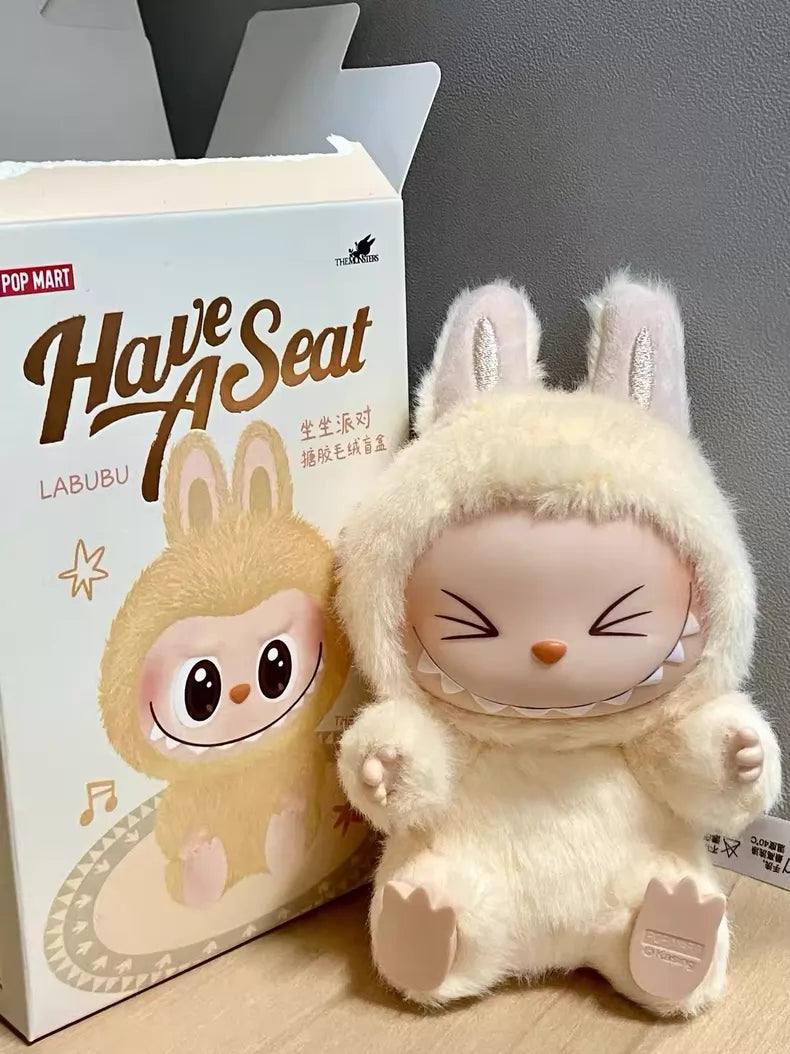 The Labubu “Sisi” Plush Keychain – Have a Seat Series Yellow Bunny by POP MART The Monsters sits beside its box on a wooden surface, adding a cute touch to your collection.
